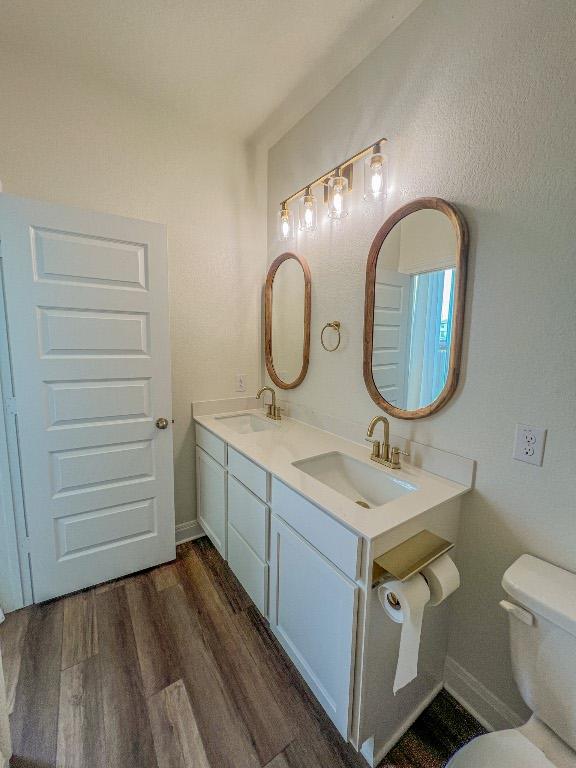bathroom featuring double vanity, a sink, wood finished floors, and toilet