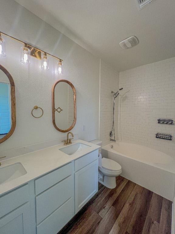 full bathroom featuring double vanity, wood finished floors, toilet, bathtub / shower combination, and a sink