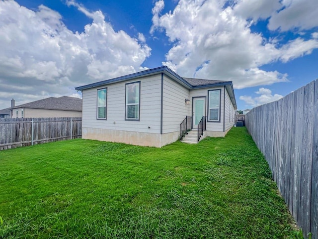 rear view of property featuring entry steps, a yard, and a fenced backyard