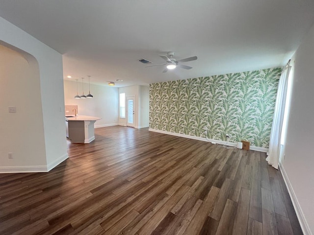 unfurnished living room featuring baseboards, an accent wall, and wallpapered walls