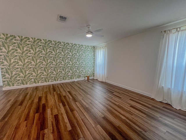 empty room featuring ceiling fan, wallpapered walls, baseboards, wood finished floors, and visible vents