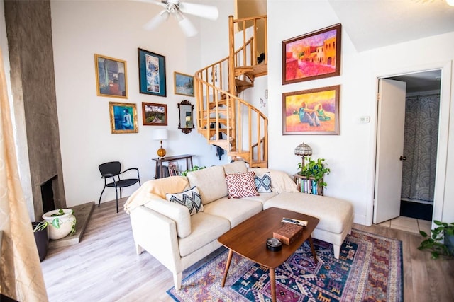 living area featuring stairs, ceiling fan, wood finished floors, and a fireplace