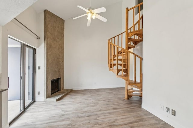 unfurnished living room with a towering ceiling, wood finished floors, stairway, a large fireplace, and a ceiling fan