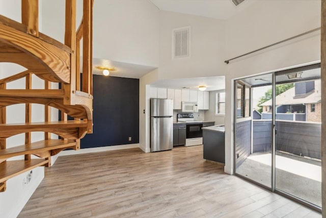interior space featuring visible vents, freestanding refrigerator, a towering ceiling, white microwave, and electric stove