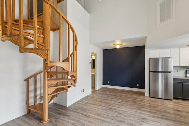 interior space featuring baseboards, a high ceiling, wood finished floors, and visible vents