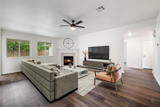 living room with a lit fireplace, ceiling fan, visible vents, and dark wood-type flooring