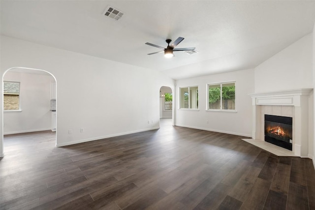 unfurnished living room featuring visible vents, ceiling fan, dark wood-style floors, a tile fireplace, and arched walkways