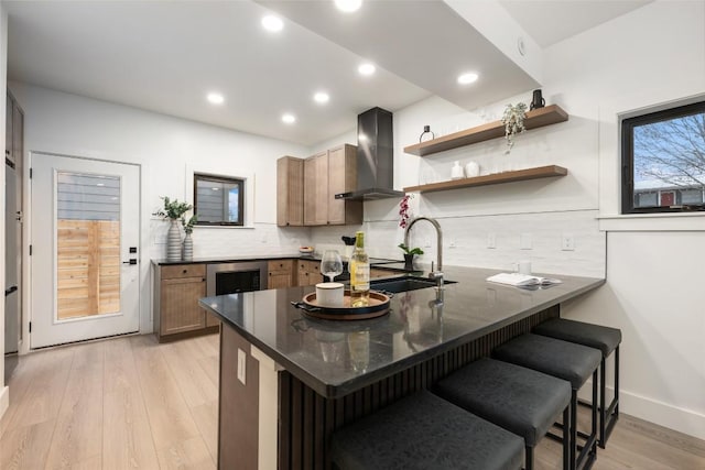 kitchen with a sink, backsplash, a kitchen bar, and wall chimney exhaust hood