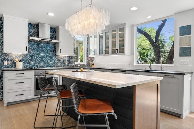 kitchen with a breakfast bar area, light wood-type flooring, a sink, wall chimney exhaust hood, and oven