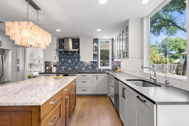 kitchen featuring wall chimney range hood, brown cabinets, appliances with stainless steel finishes, a sink, and tasteful backsplash