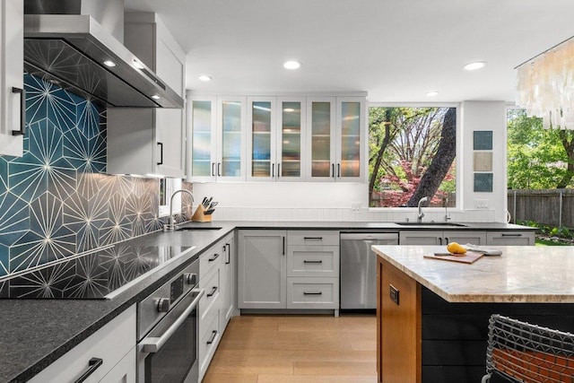 kitchen featuring wall chimney range hood, stainless steel appliances, recessed lighting, and a sink