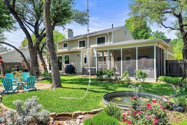 rear view of property featuring fence, a yard, a chimney, and a sunroom