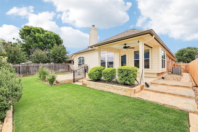rear view of property featuring ceiling fan, a fenced backyard, a gate, a chimney, and a lawn