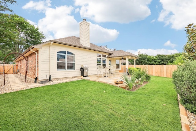 rear view of house with a patio, a fenced backyard, a chimney, a ceiling fan, and a yard