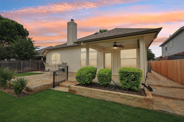 back of property at dusk featuring a patio, a ceiling fan, a lawn, and fence
