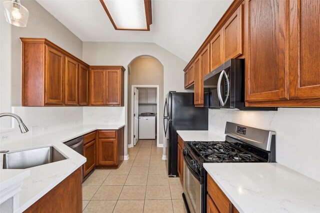kitchen featuring washer / dryer, a sink, appliances with stainless steel finishes, light tile patterned floors, and vaulted ceiling