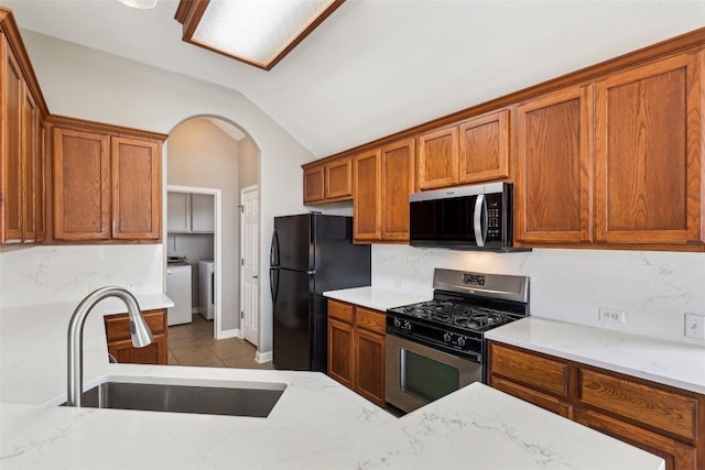 330 Wildhorse Crk, Buda, TX 78610 - kitchen with appliances with stainless steel finishes, washer and clothes dryer, a sink, lofted ceiling, and brown cabinetry
