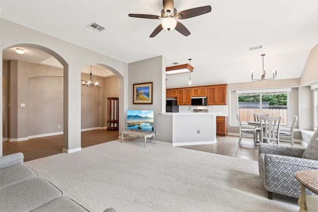 living area featuring light colored carpet, arched walkways, visible vents, and ceiling fan with notable chandelier