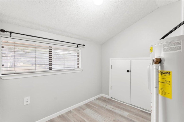 unfurnished room featuring light wood finished floors, a textured ceiling, water heater, baseboards, and vaulted ceiling