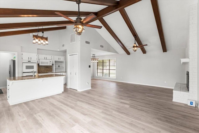 unfurnished living room featuring beamed ceiling, a fireplace, ceiling fan with notable chandelier, and light wood-type flooring