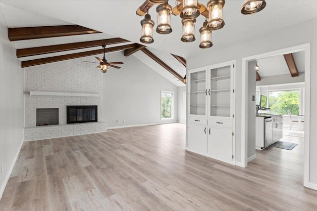 unfurnished living room featuring vaulted ceiling with beams, a healthy amount of sunlight, ceiling fan with notable chandelier, and light wood-style floors
