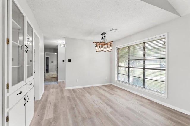 unfurnished dining area featuring a textured ceiling, a chandelier, baseboards, and light wood-style floors