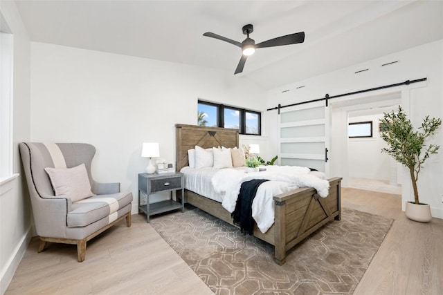 bedroom with multiple windows, a barn door, light wood finished floors, and lofted ceiling