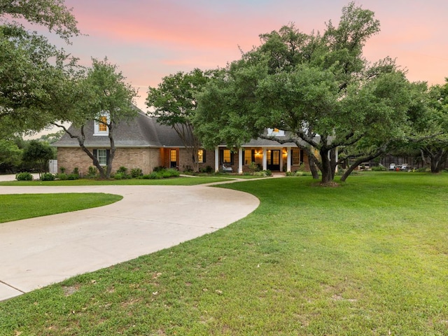 view of front of house with curved driveway, a front lawn, covered porch, and brick siding