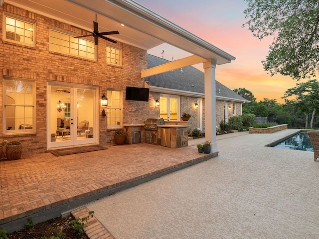 rear view of property with ceiling fan, an outdoor kitchen, a fenced in pool, brick siding, and a patio area