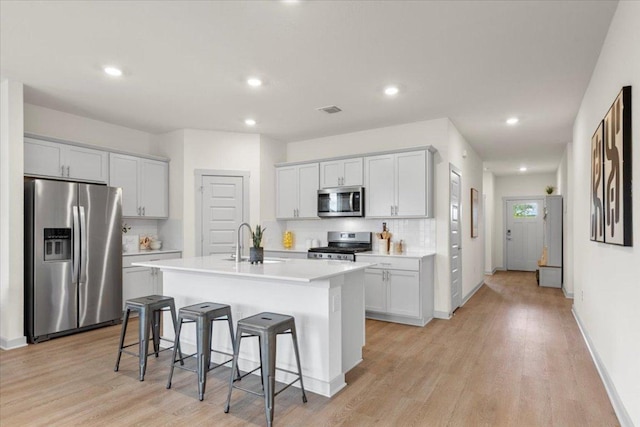 kitchen featuring a sink, light wood finished floors, a breakfast bar area, stainless steel appliances, and decorative backsplash