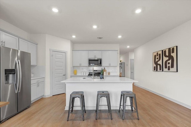 kitchen with a kitchen breakfast bar, appliances with stainless steel finishes, tasteful backsplash, light countertops, and light wood finished floors