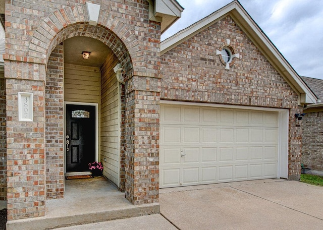 doorway to property with an attached garage, driveway, and brick siding