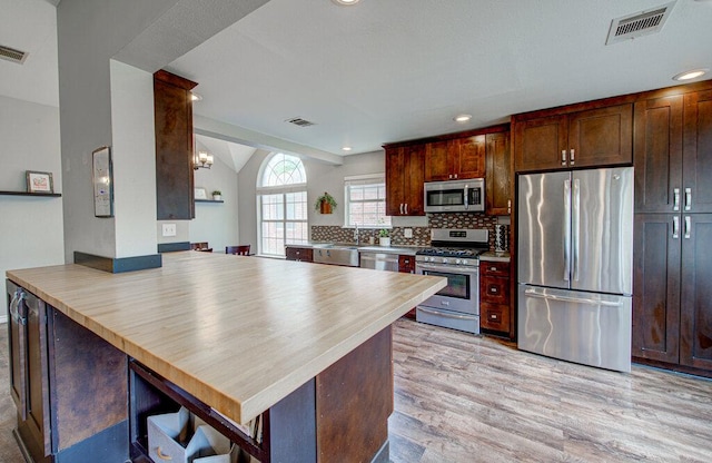 kitchen featuring decorative backsplash, visible vents, vaulted ceiling, light wood-style floors, and stainless steel appliances