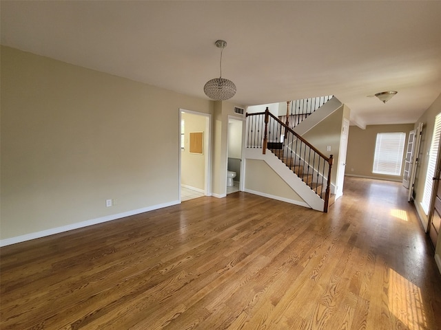 unfurnished living room featuring baseboards, visible vents, wood finished floors, and stairway