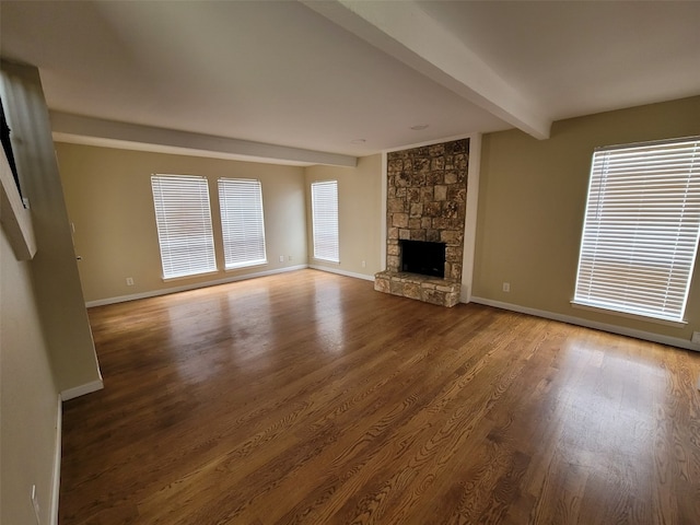 unfurnished living room featuring baseboards, beamed ceiling, a stone fireplace, and wood finished floors