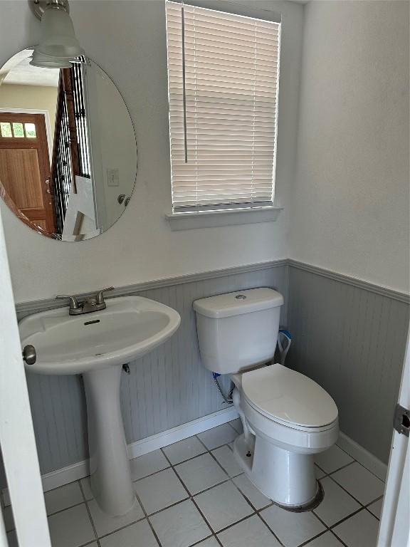 half bath featuring wainscoting, a sink, toilet, tile patterned floors, and baseboards