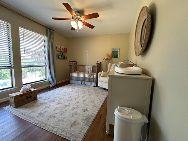 bedroom featuring a crib, ceiling fan, baseboards, and wood finished floors