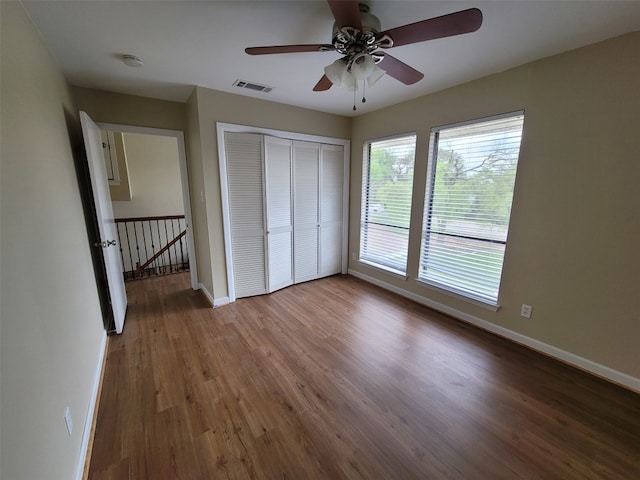 unfurnished bedroom with ceiling fan, visible vents, wood finished floors, baseboards, and a closet