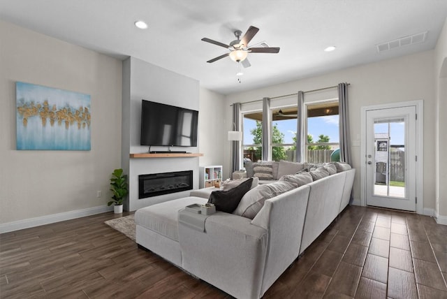 living area with ceiling fan, visible vents, a glass covered fireplace, and dark wood finished floors
