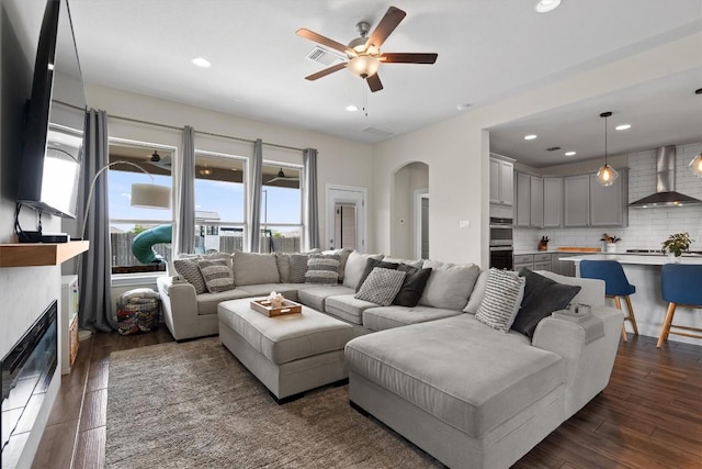 living room with ceiling fan, arched walkways, a glass covered fireplace, dark wood-type flooring, and visible vents