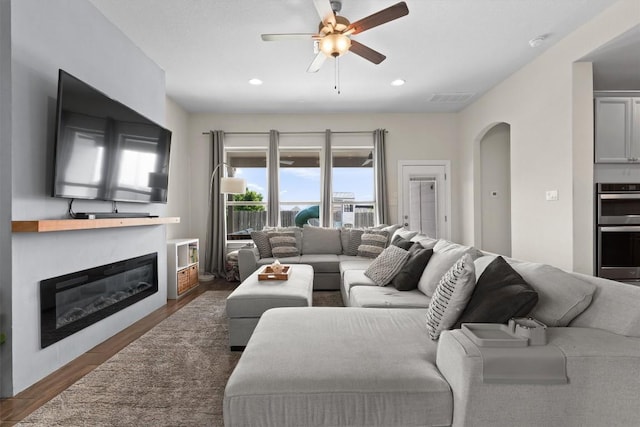 living area with a ceiling fan, visible vents, arched walkways, wood finished floors, and a glass covered fireplace