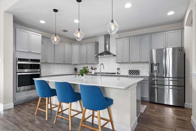 kitchen with wall chimney range hood, gray cabinetry, stainless steel appliances, and dark wood finished floors