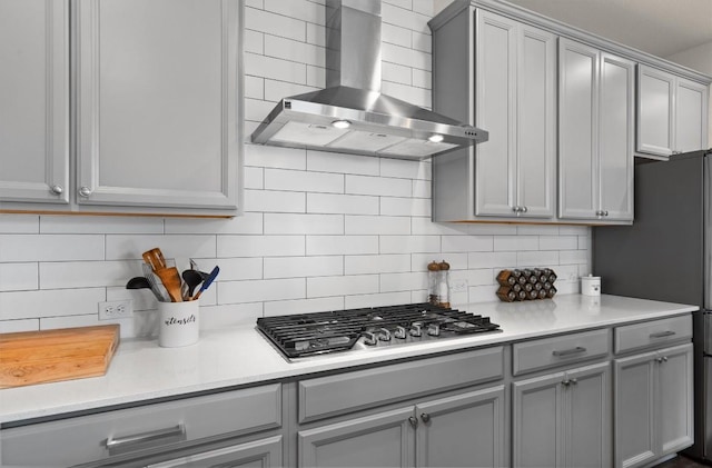 kitchen featuring decorative backsplash, stainless steel gas cooktop, light countertops, wall chimney exhaust hood, and gray cabinetry