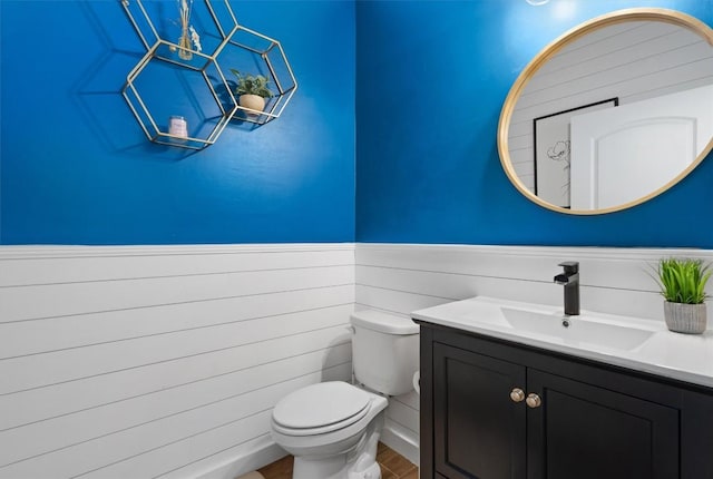 half bathroom featuring a wainscoted wall, vanity, toilet, and wood finished floors