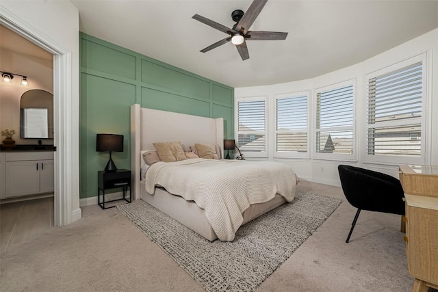 bedroom with a ceiling fan, baseboards, light carpet, a decorative wall, and ensuite bath