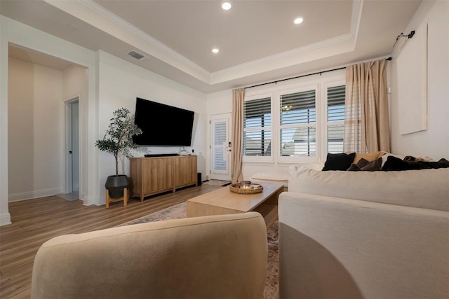 living area featuring a raised ceiling, baseboards, wood finished floors, visible vents, and ornamental molding