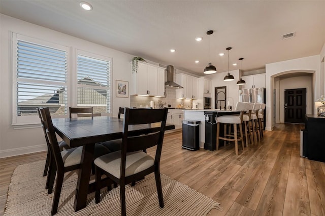 dining area featuring visible vents, arched walkways, light wood-style flooring, and recessed lighting