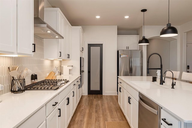 kitchen featuring appliances with stainless steel finishes, a sink, light wood-style flooring, wall chimney exhaust hood, and white cabinetry