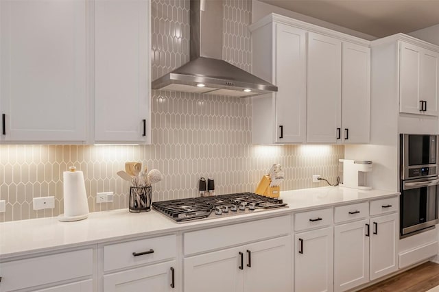 kitchen with wall chimney range hood, stainless steel appliances, white cabinetry, and light countertops