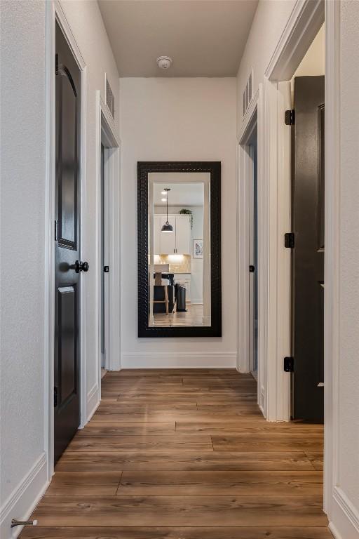 corridor featuring baseboards, visible vents, and wood finished floors